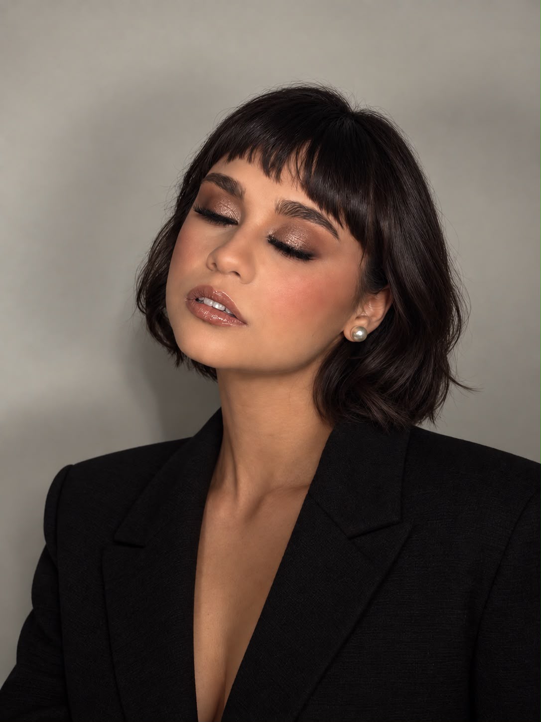 Maquillaje editorial en tonos cobre con glitter en el párpado y labios nude glossy, sobre melena bob con fleco.