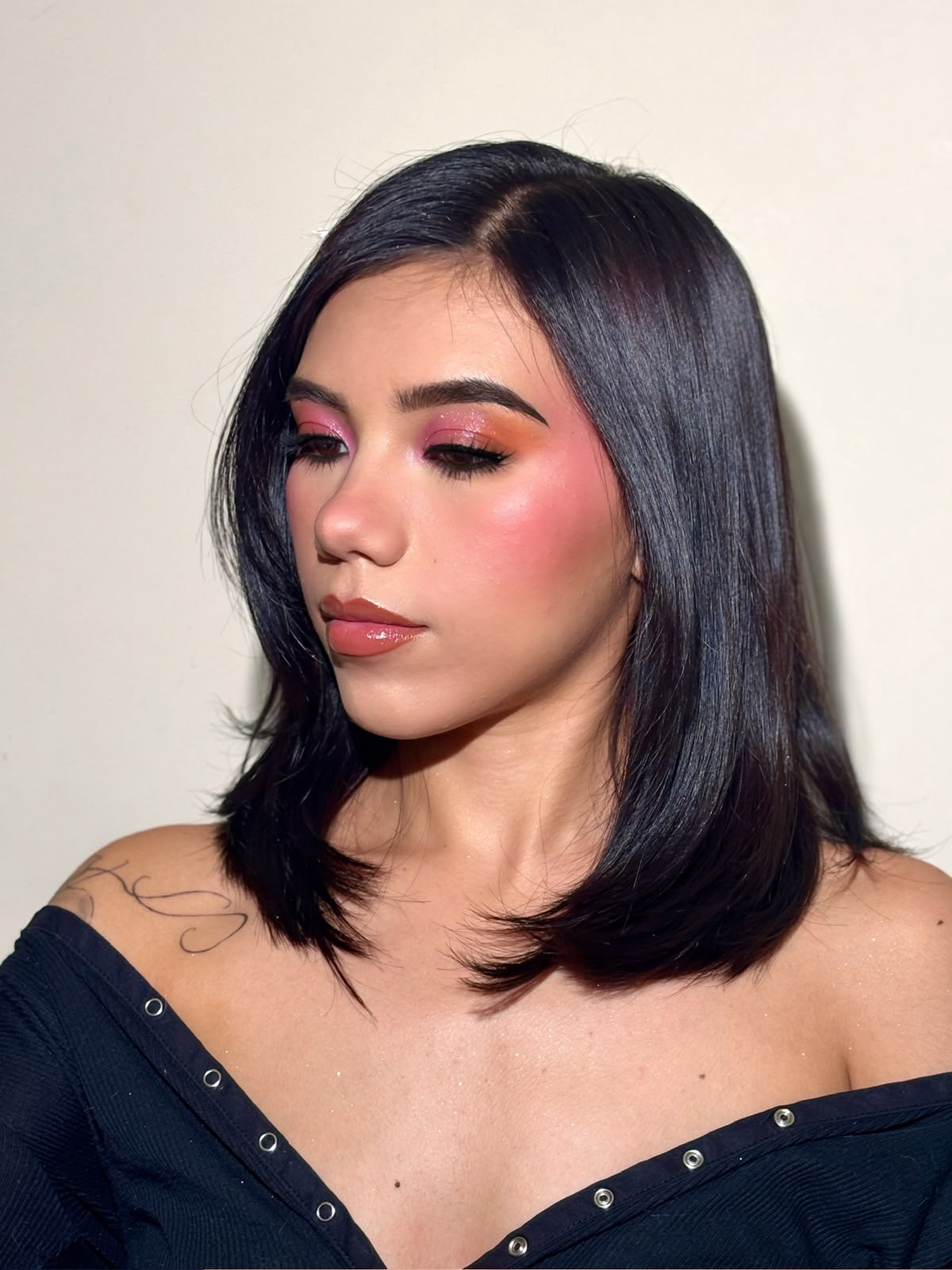 Maquillaje en tonos rosa y coral con rubor difuminado y delineado negro, sobre cabello lacio oscuro.